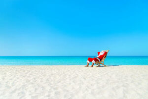 Christmas Santa Claus resting on deckchair at ocean sandy tropical beach - xmas travel vacation in hot countries concept